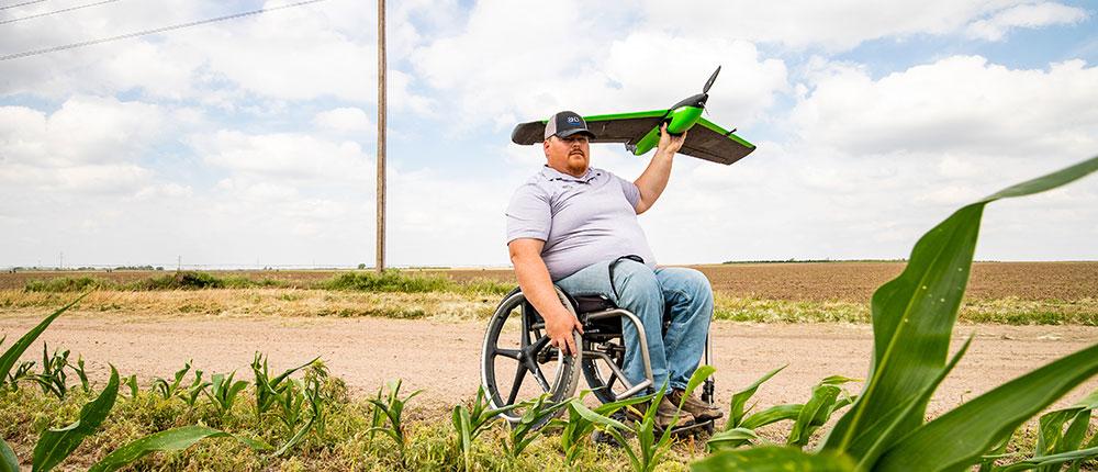 Man in wheelchair gets ready to launch a drone over farm fields.
